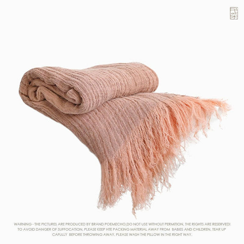Folded blush pink linen throw blanket with textured weave and delicate fringes.