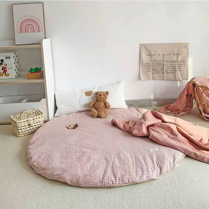 Round pink and white gingham play mat with a teddy bear and draped pink muslin blanket.