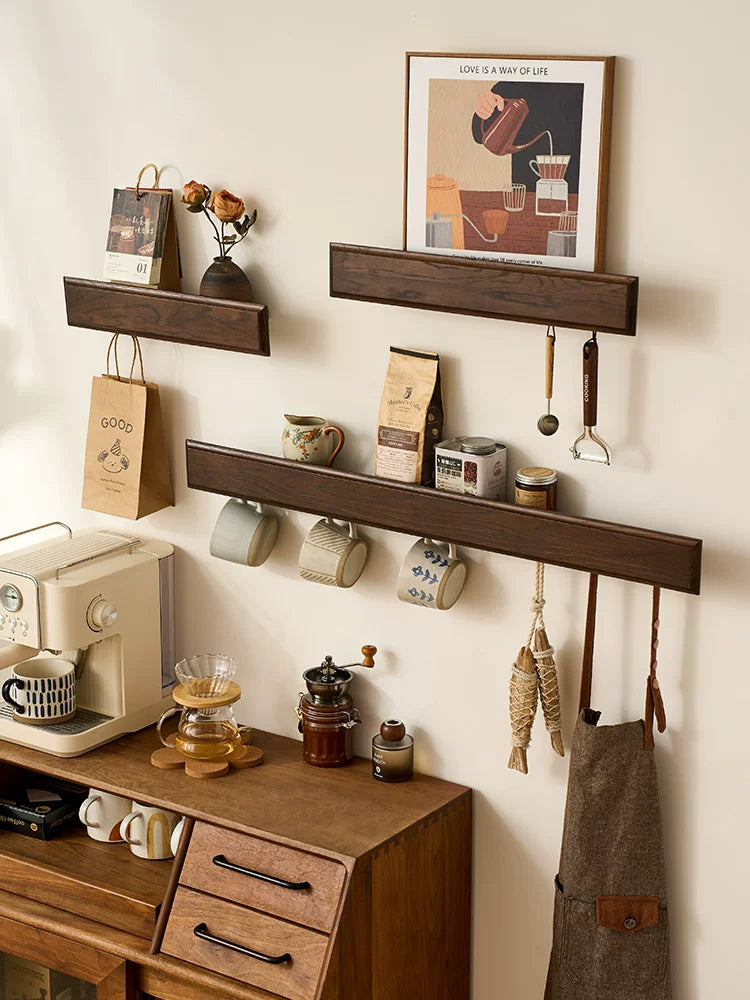 Dark wood wall shelves used as coffee station storage with mugs, coffee beans, and apron.