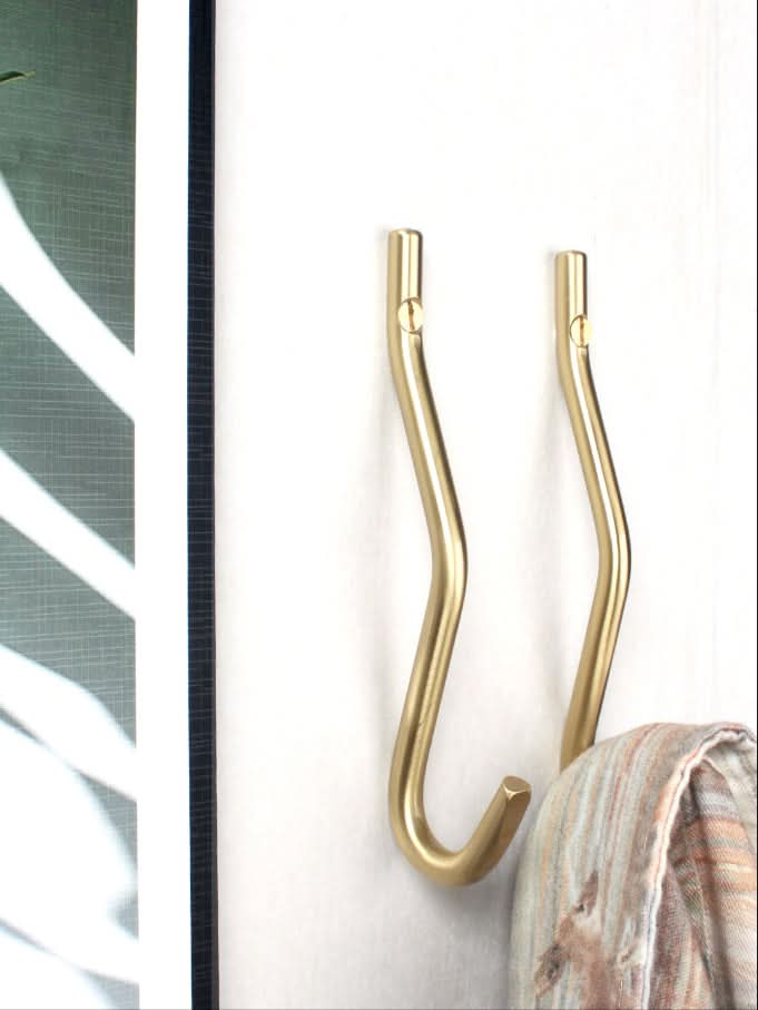 Minimalist brass wall hooks with a scarf hanging on one hook.