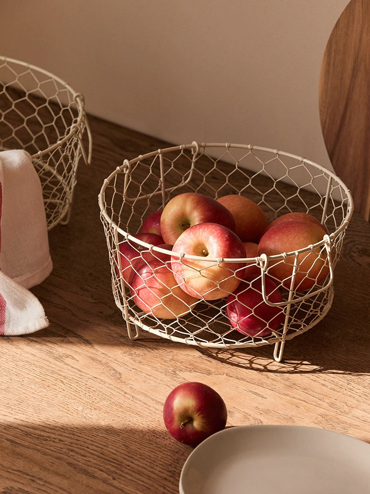Beige wire dish basket with handles, filled with apples.  Rustic, honeycomb-patterned wire. Kitchen storage.