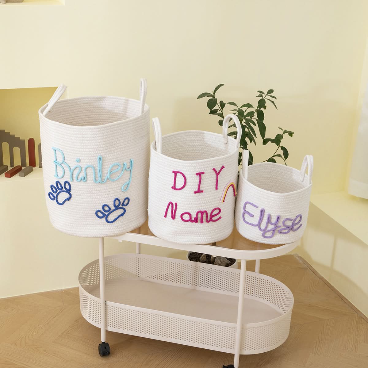 Personalized Name Woven Storage Baskets: White rope baskets with blue, pink, and purple embroidered names and paw prints.