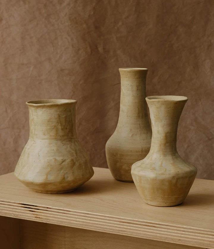 A small, hand-thrown ceramic vase with a textured, creamy white and beige curd glaze.