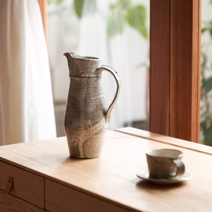 Ceramic jug with rough pottery glaze in earthy tones, set on a wooden surface.