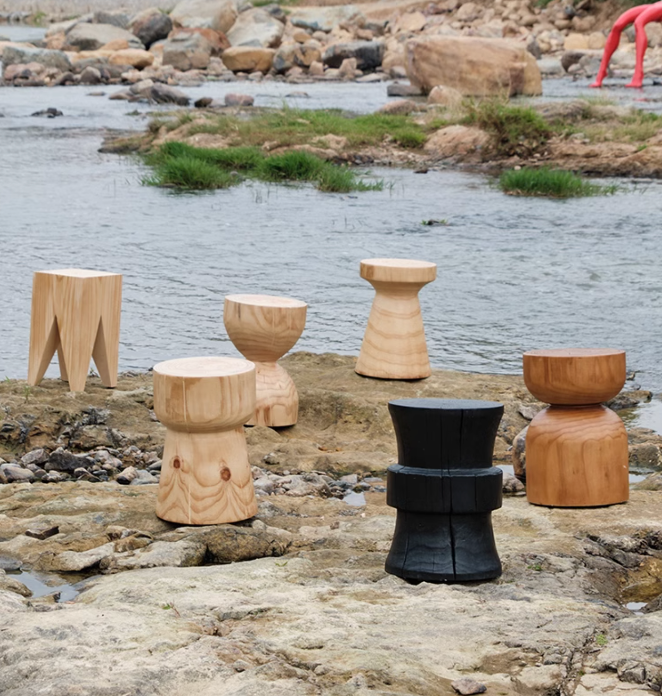 Various solid wood stools, customizable size, displayed outdoors by a river on rocks.