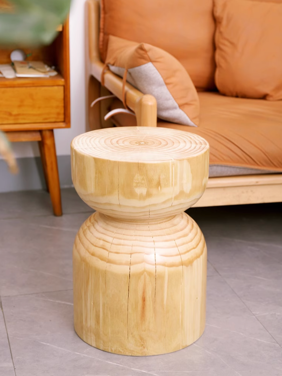 Natural wood stool with hourglass shape, customizable size, shown in a modern living room setting.