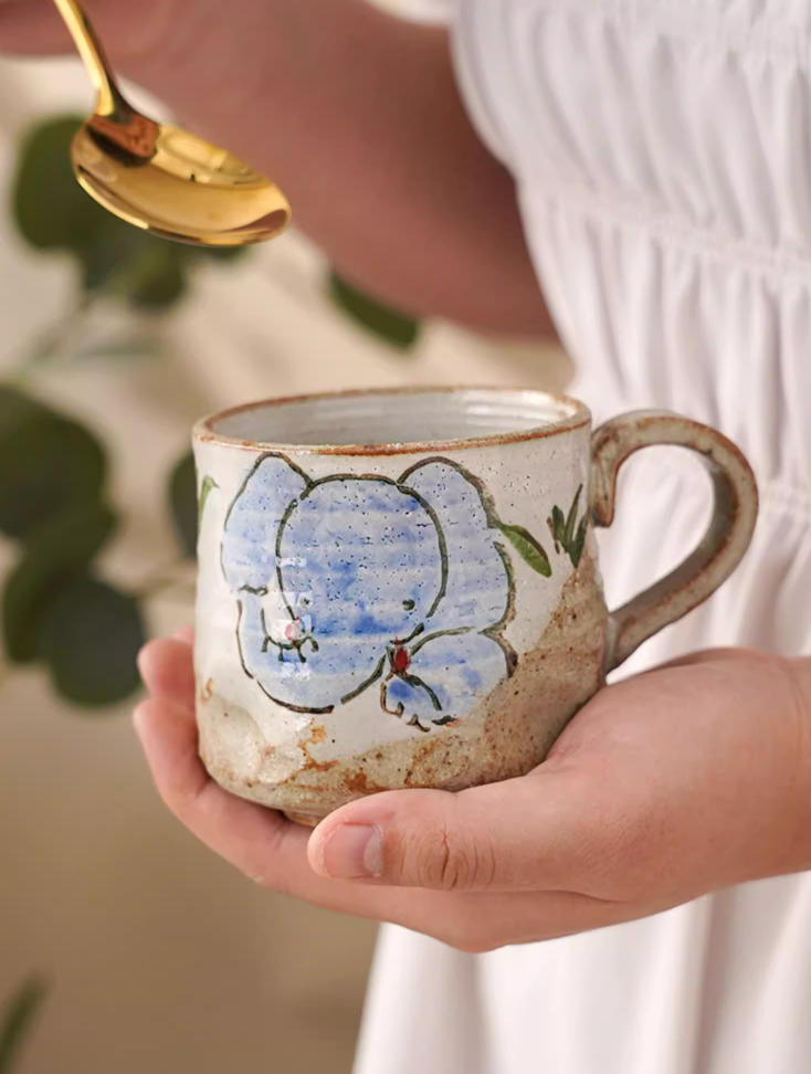 Hand painted ceramic 11oz coffee mug with blue floral design, held by hands.