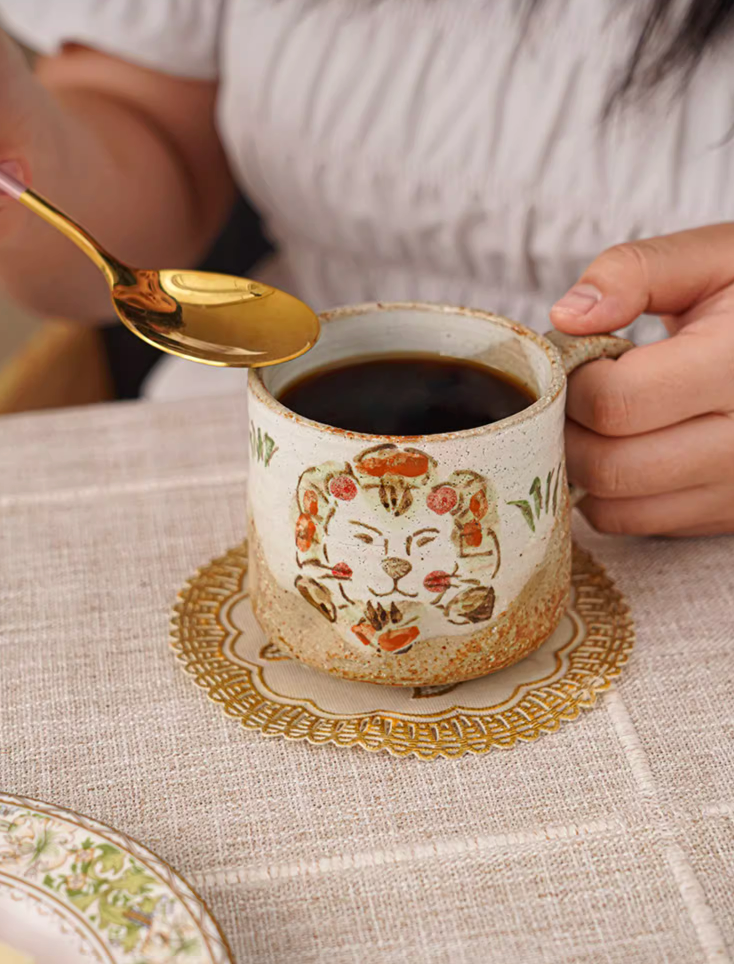 Hand painted coffee mug 11oz with lion design on beige textured ceramic, on linen tablecloth.