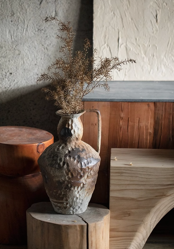 Wabi-Sabi distressed rustic vase with dried branches, earthy tones on textured background.