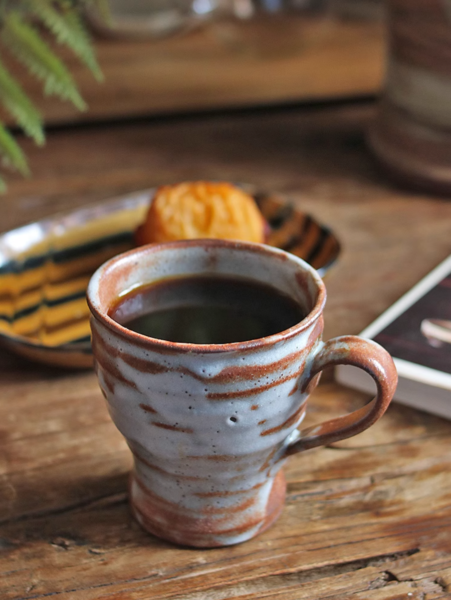 Handmade ceramic coffee mug with a marbled glaze on a rustic wooden table.