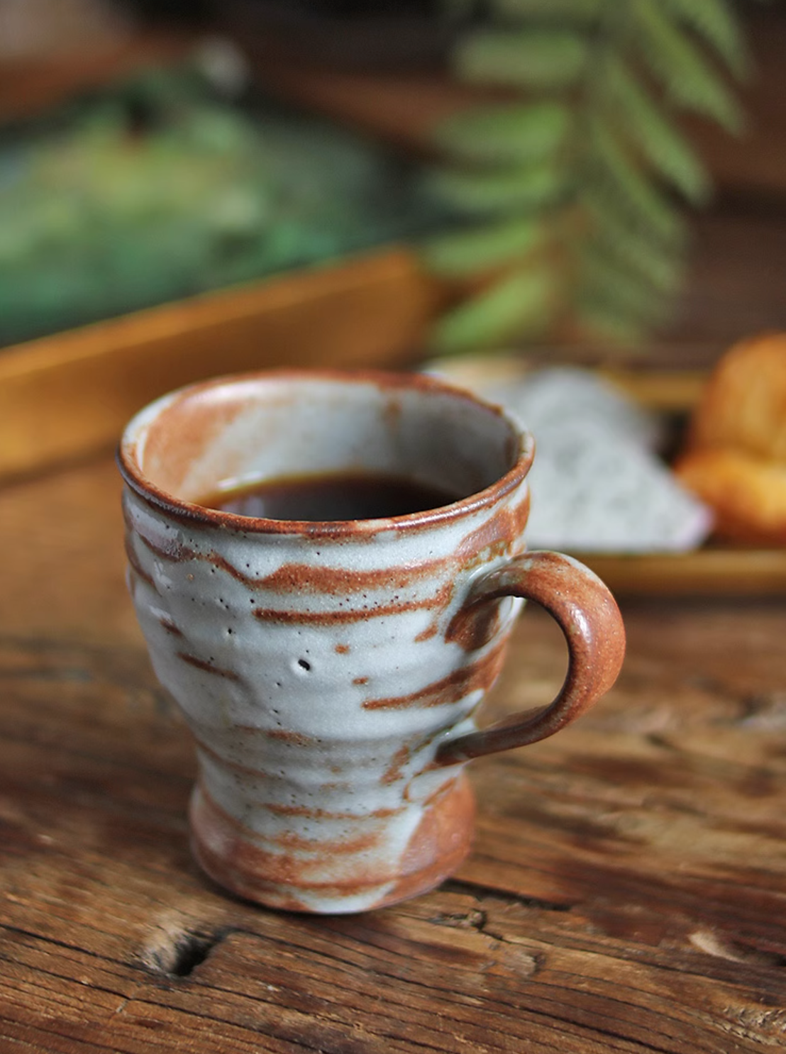 Handmade ceramic coffee mug with rustic brown and white glaze, filled with coffee, on a wooden table.