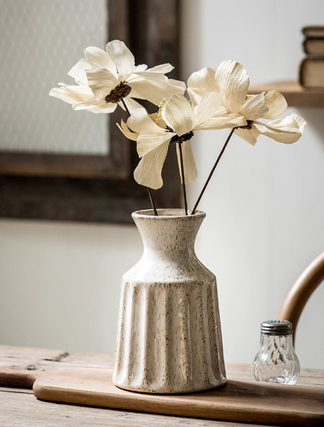 Textured white ceramic small vase holding light-colored flowers on wooden table.