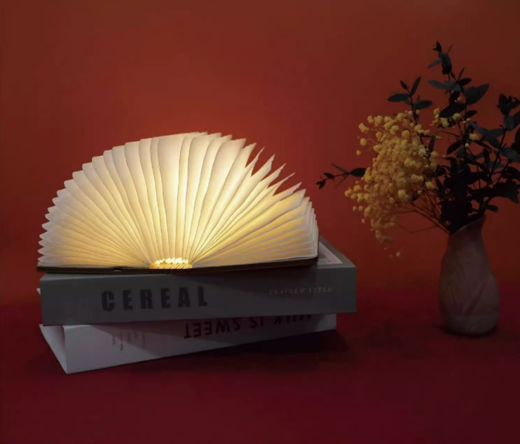 Glowing customizable book paper table lamp on stacked books, with yellow flowers in a vase.