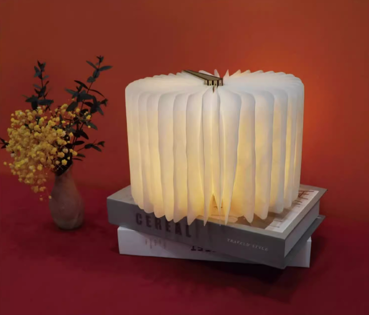 Illuminated white paper Customizable Book Paper Table Lamp on stacked books with floral decor.
