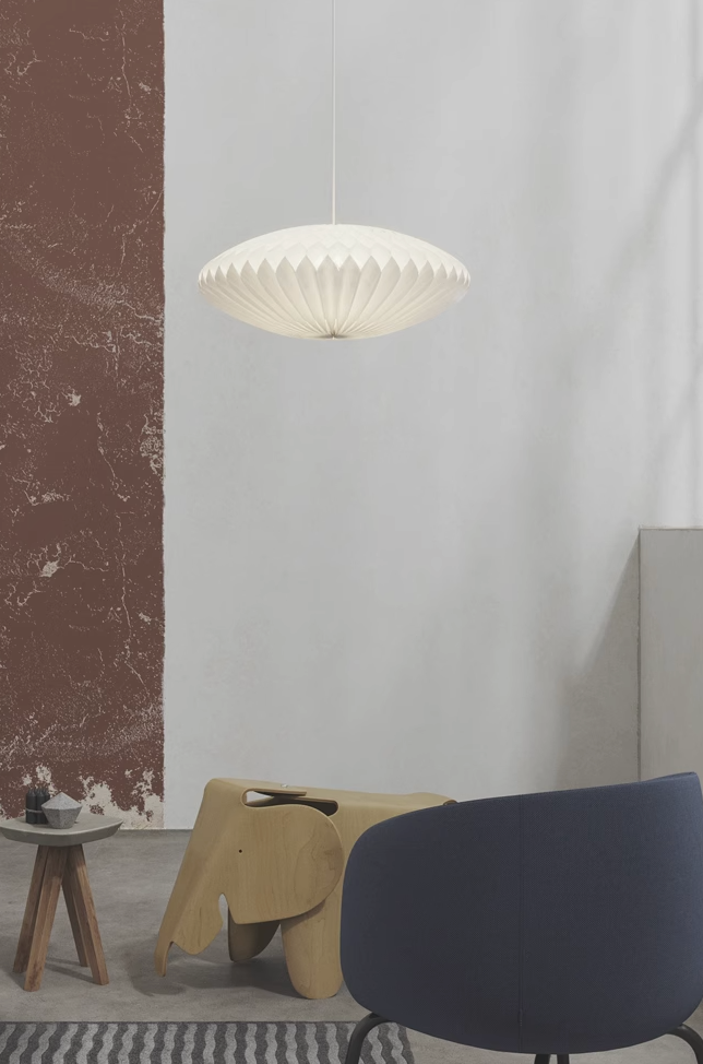 White geometric origami paper lampshade hanging above wooden elephant stool in minimalist home decor setting.