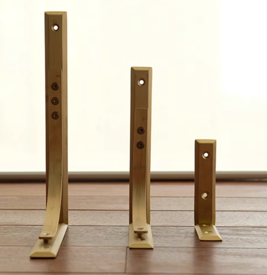 Three brass shelf brackets in varying sizes on a wooden floor.