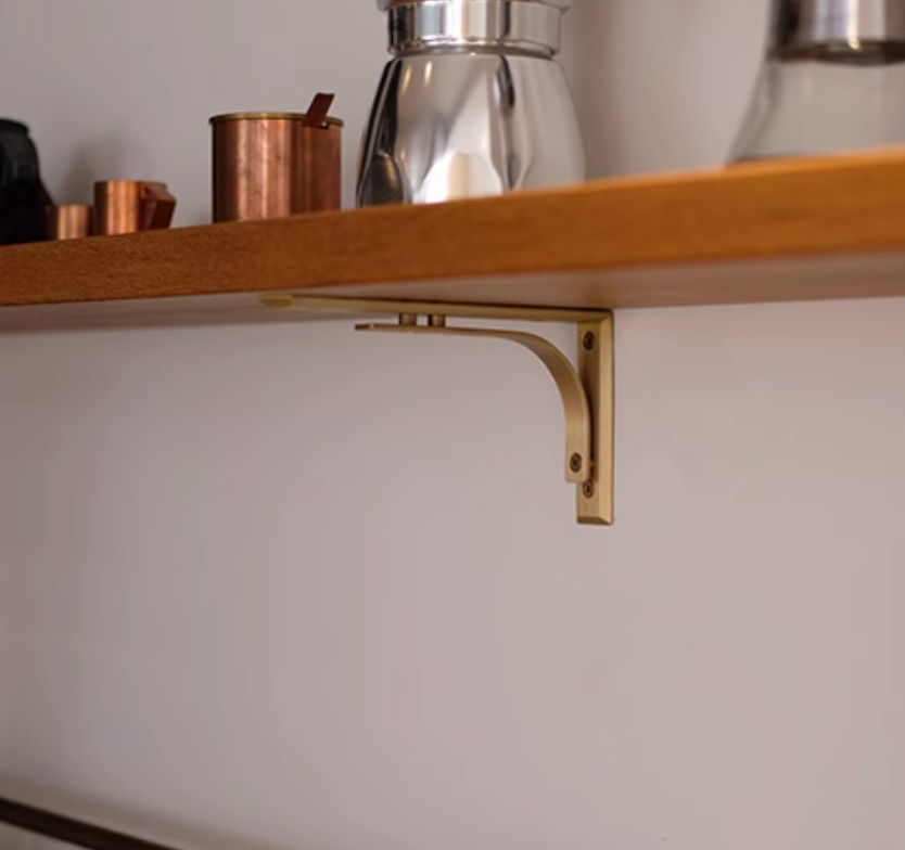 Brass shelf bracket supporting a wooden shelf with copper and silver decor.