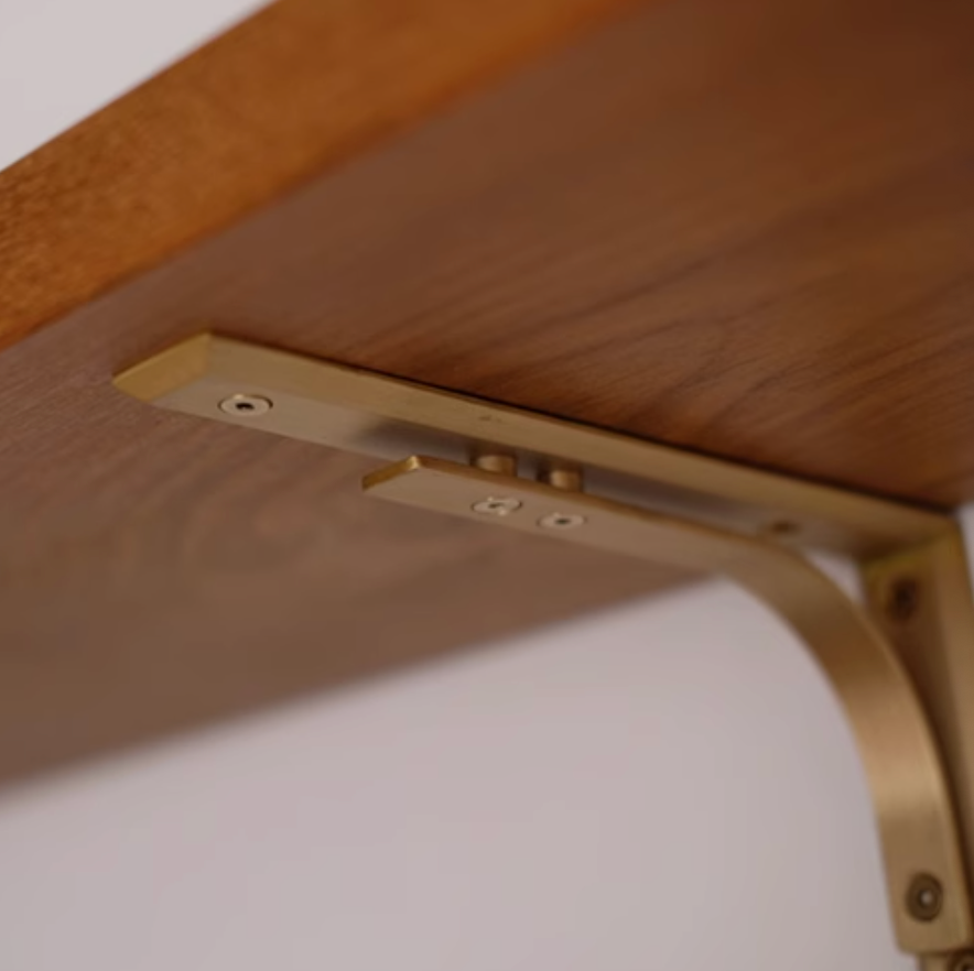 Brass shelf bracket installed on a wooden shelf, featuring a brushed gold finish.