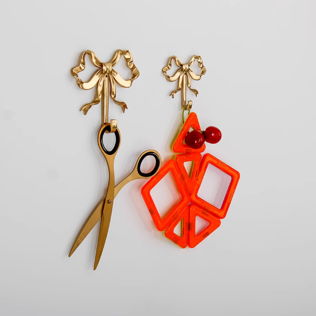 Golden brass tie wall hook with bow detail, holding scissors and colorful decor.
