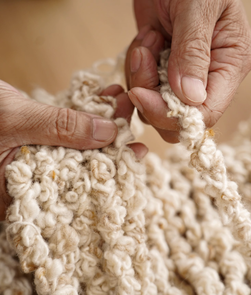 Hands weaving a cream-colored hand-woven wool shaggy rug, showcasing natural fibers.