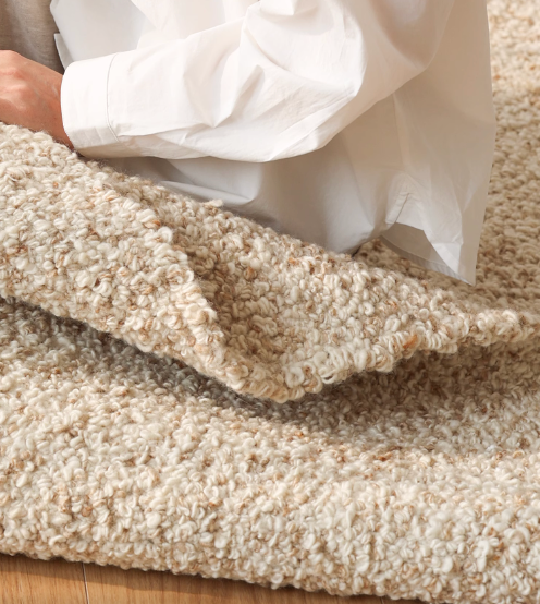 Cream hand-woven wool shaggy rug with textured loops, on a wooden floor.