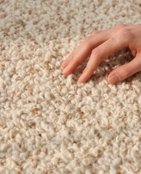 Hand-woven wool shaggy rug in cream and tan, showing texture with a person's hand.