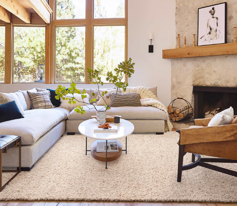 Cream hand-woven wool shaggy rug in a cozy living room setting with a sectional sofa and fireplace.