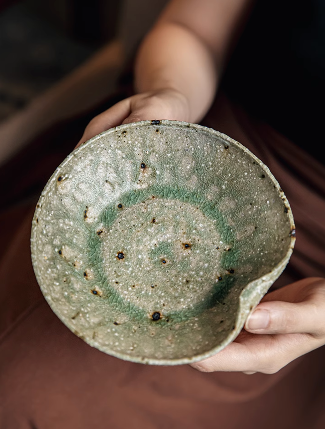 Artisan Green Dinnerware: Speckled ceramic bowl with a textured green glaze, held by hands.