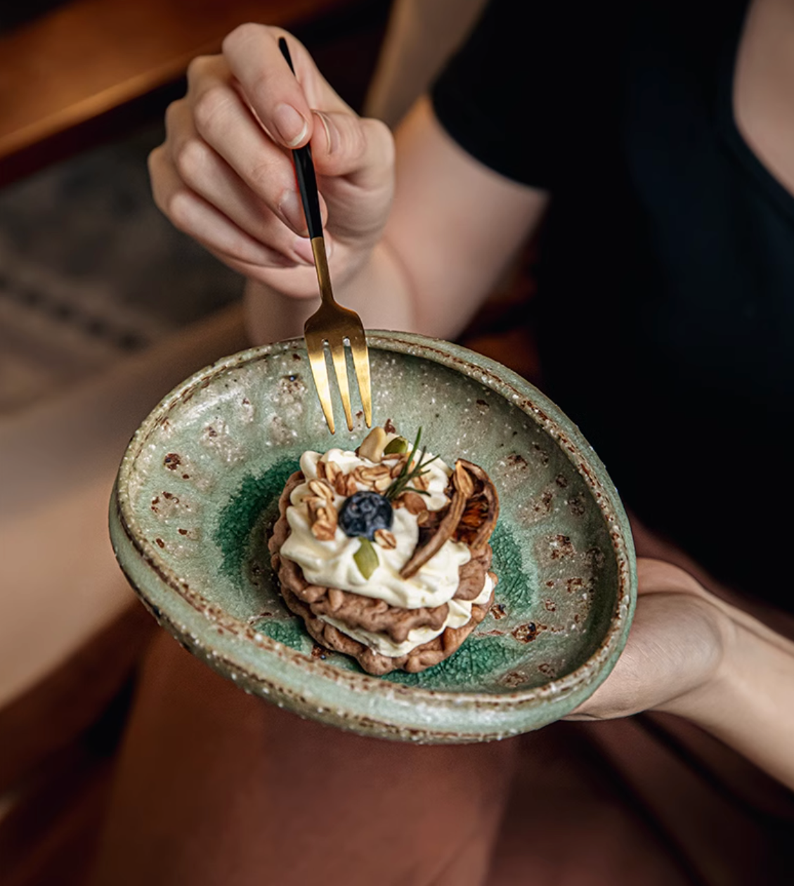 Artisan Green Dinnerware: textured ceramic bowl holding a gourmet dessert, presented by a hand with a gold fork.