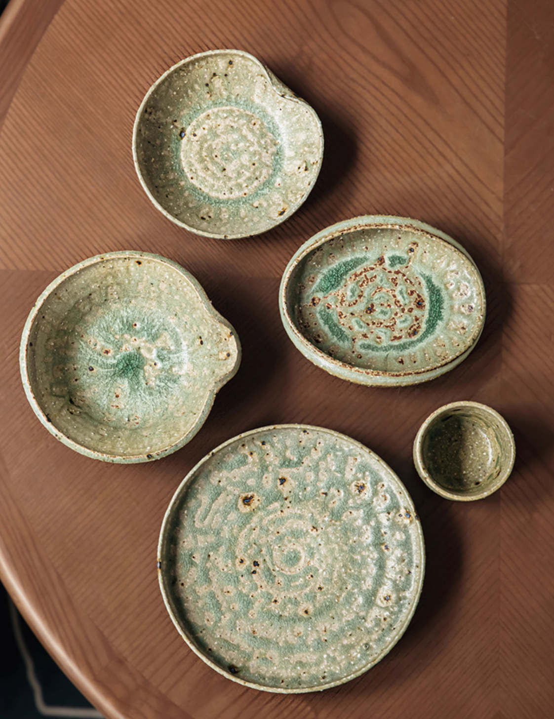 Artisan Green Dinnerware set, handcrafted ceramic plates & bowl with speckled green glaze on a wooden table.