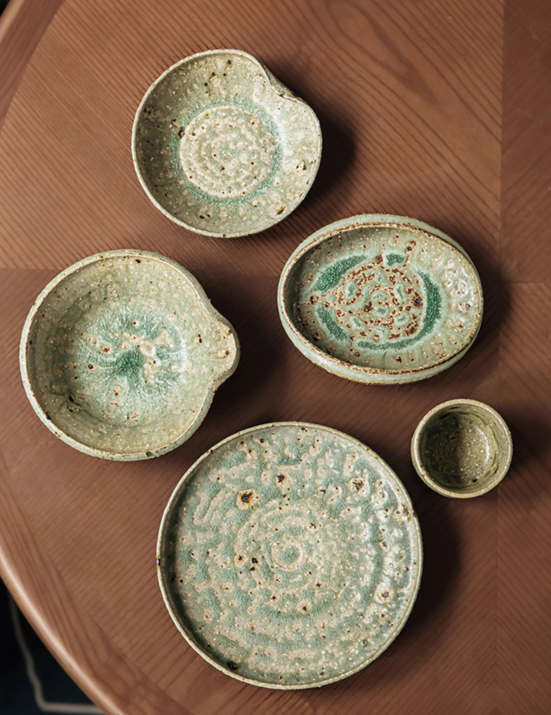 Handcrafted green and brown ceramic dinnerware set; various shapes and sizes; rustic aesthetic.