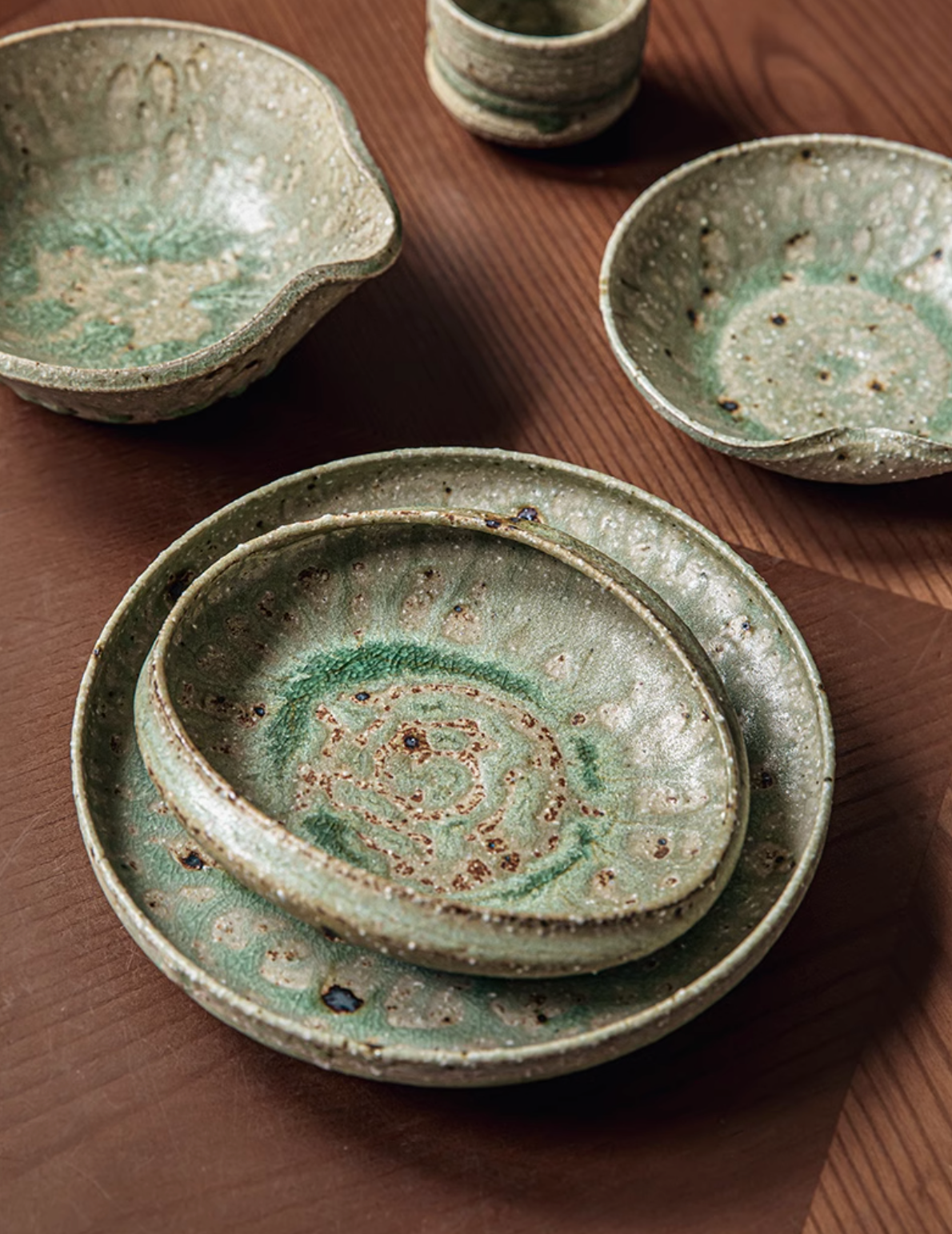 Artisan Green Dinnerware set in textured ceramic, with speckled green glaze on a wooden table.