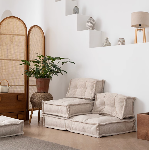 Modern beige fabric modular sofa in a living room setting with rattan screen and plant.