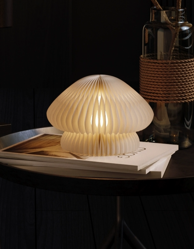 Paper Origami Mushroom Bedside Lamp, a soft ivory paper lamp glowing warmly on a book.