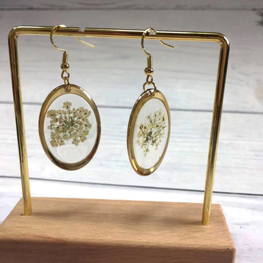 Oval gold-plated pressed flower earrings with delicate white blossoms, set in clear resin.