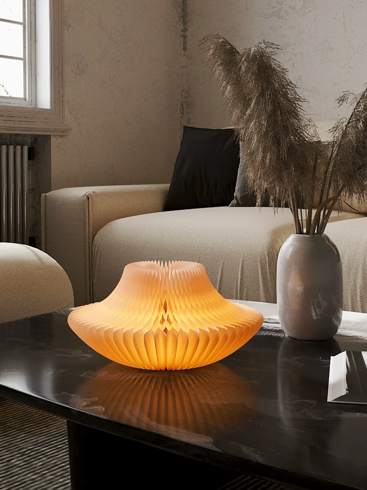 Bell-shaped origami paper lamp glowing warm orange on a dark table, home decor