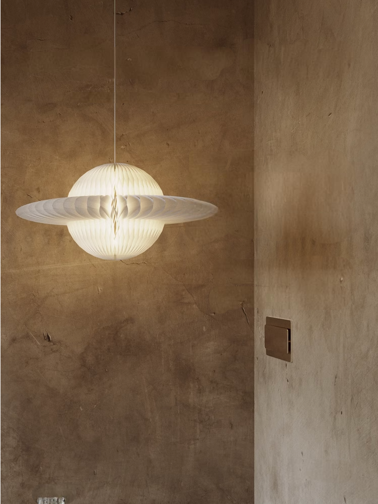 White Geometric Origami Paper Lampshade illuminates a textured brown wall.
