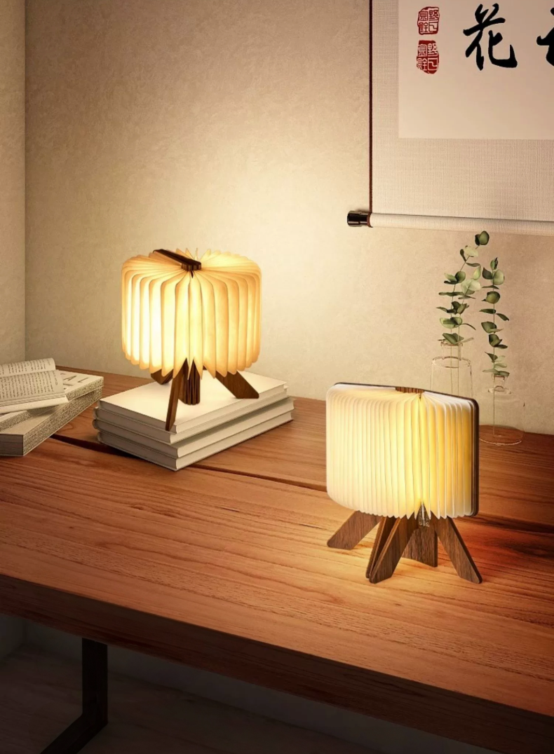 Warm, glowing folding portable paper lamp on wood desk with books.