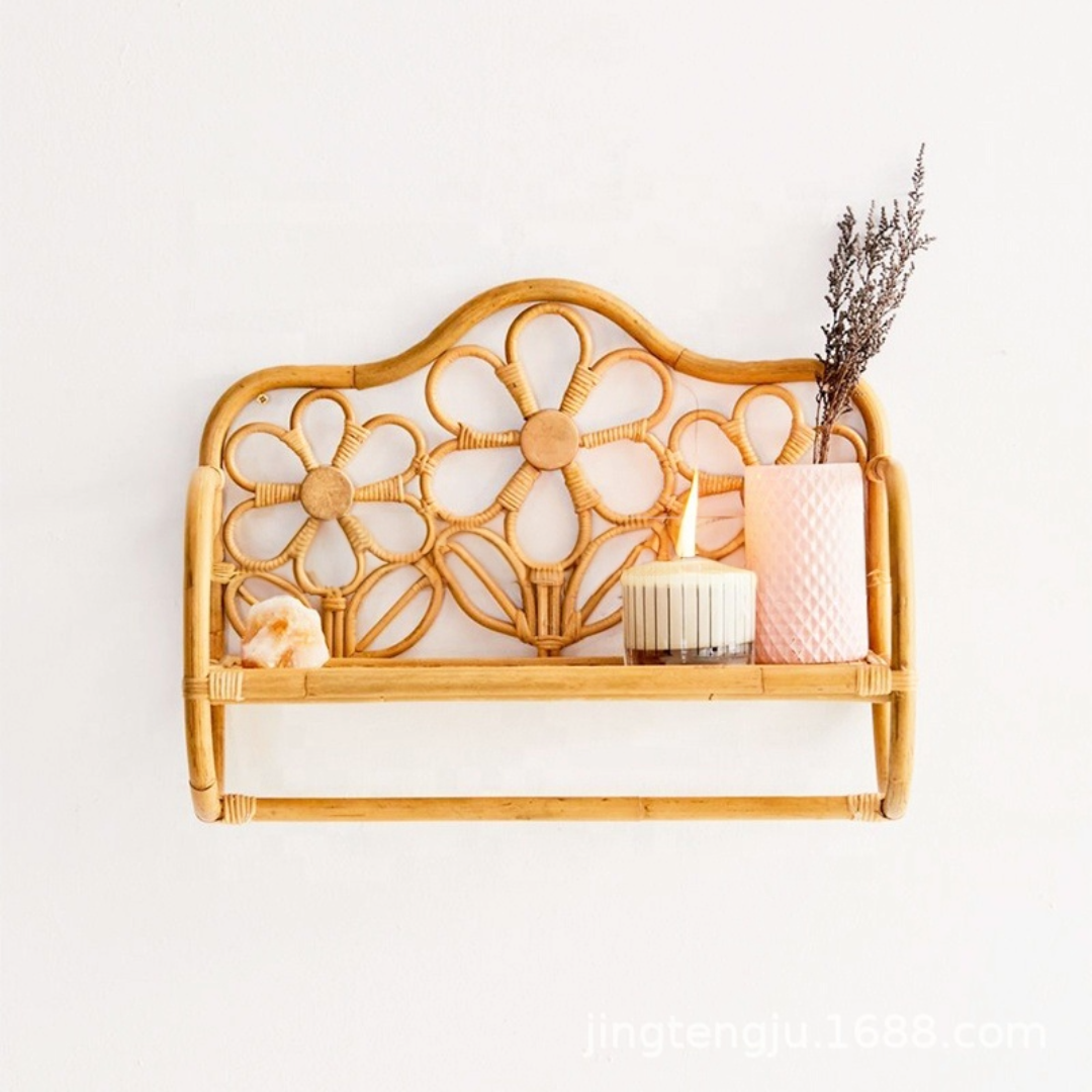 Natural rattan wall shelf with flower pattern, holding a candle, pink vase, dried plant, and crystal on a white wall.