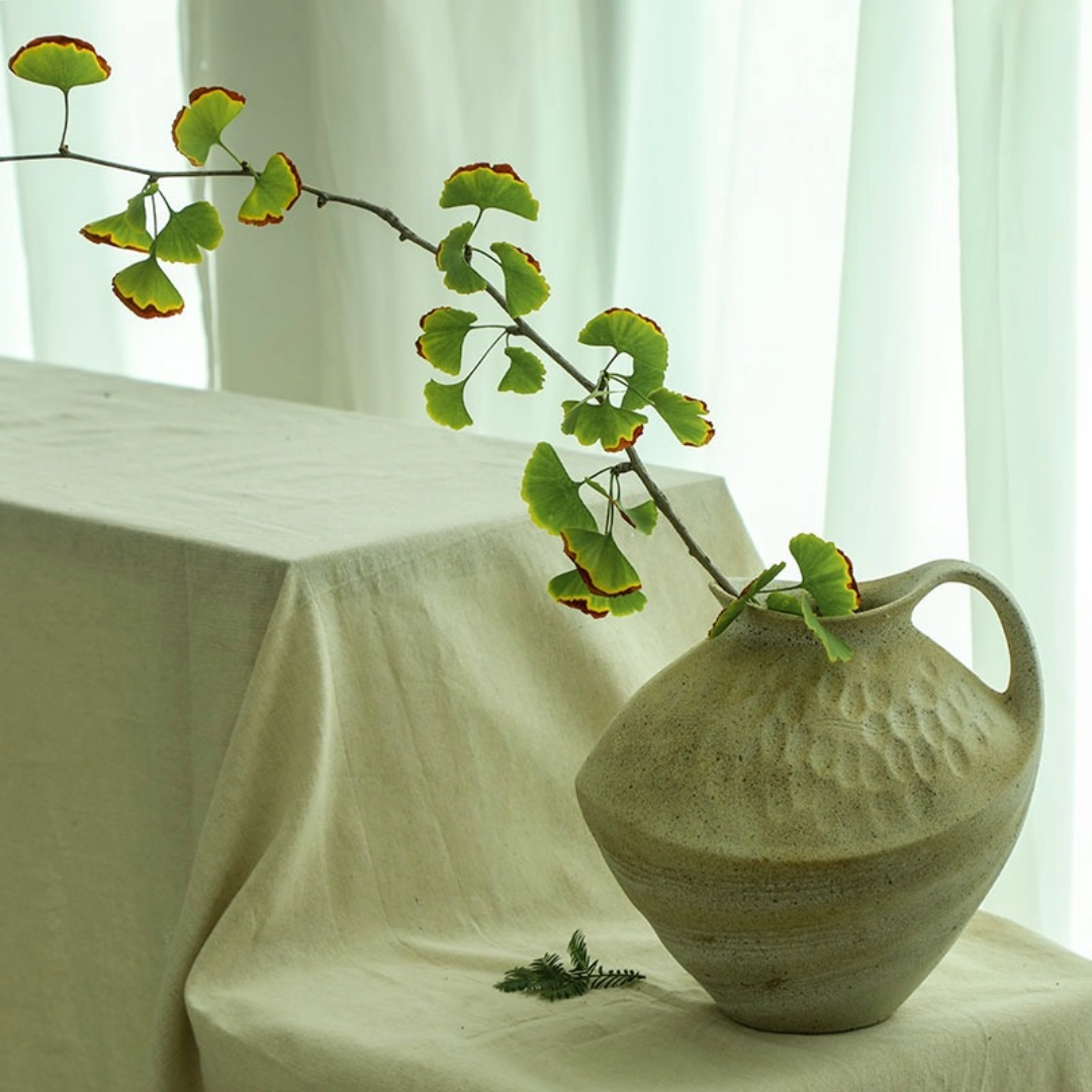 Wabi-sabi clay pot with textured finish holds ginkgo branches, natural home decor accent.