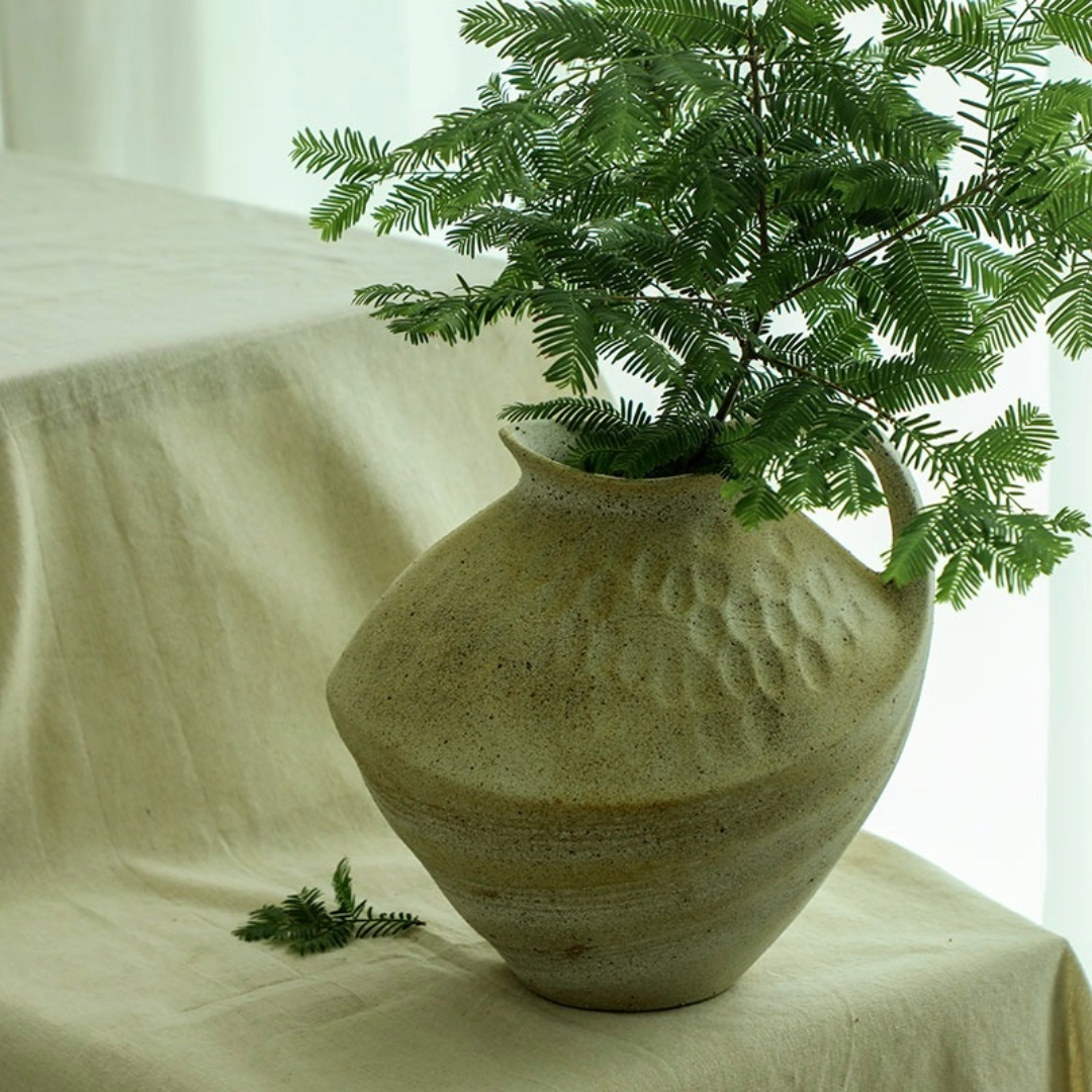 Wabi-sabi clay pot with brush effect, holding green foliage, on beige linen. Home decor.