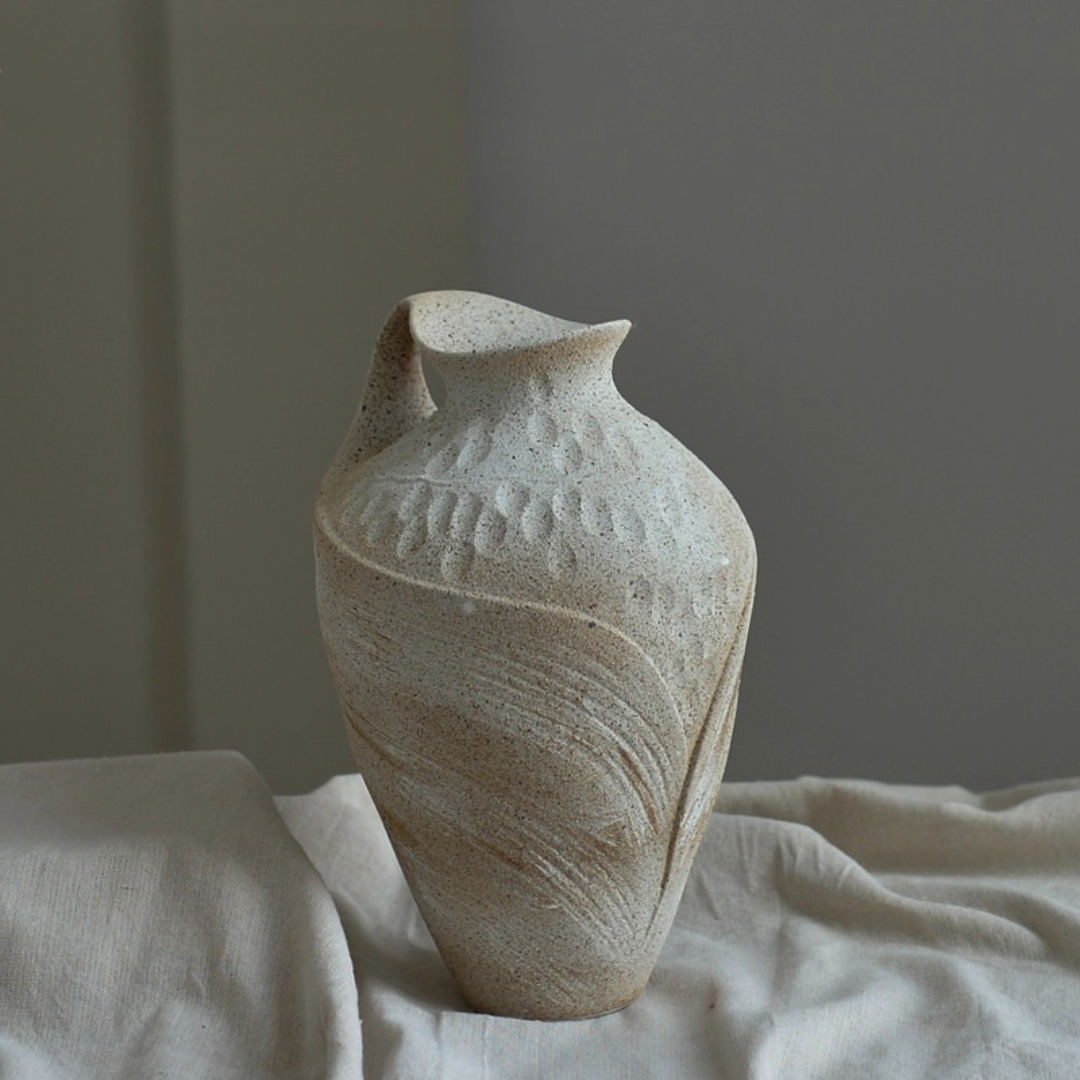 Wabi-sabi clay pot with painterly textured finish in speckled beige on draped fabric.