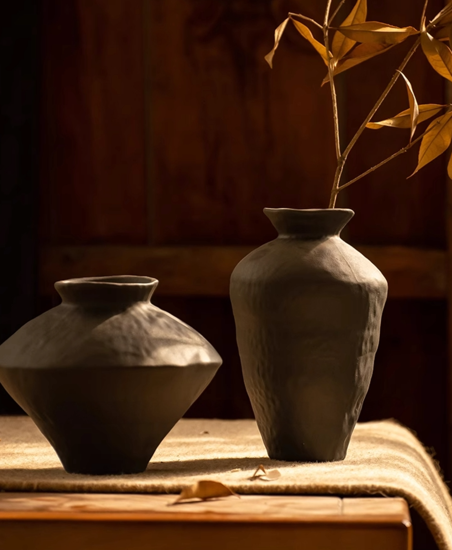 Black ceramic vases, irregular shapes, one holding dry leaves. Home decor.