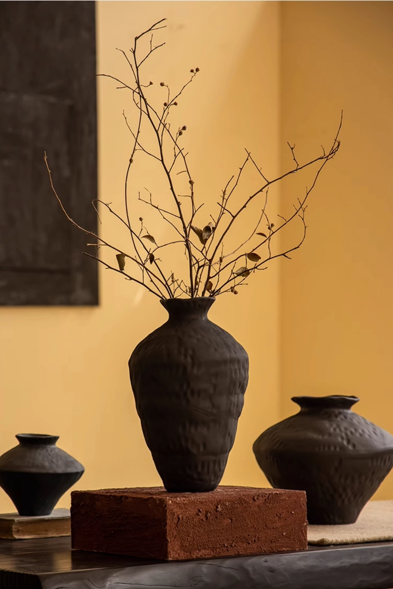 Ceramic black vase with irregular texture, holding dry branches, home decor.
