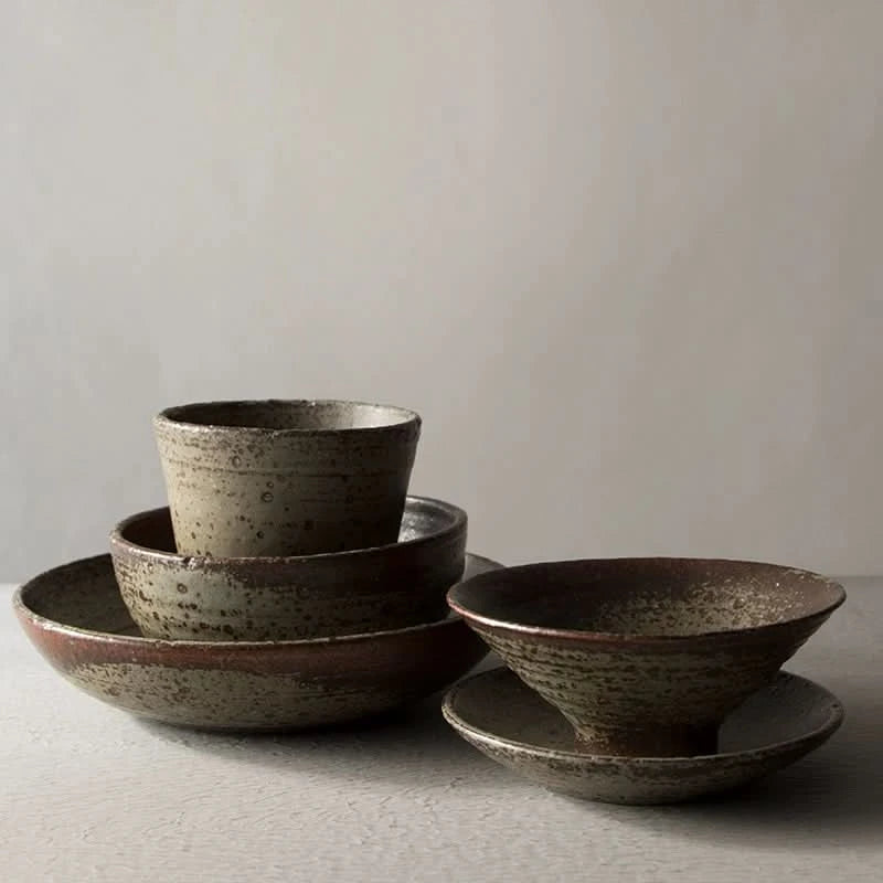 Handmade stoneware brown dinnerware set with textured bowls and plates on a light surface.