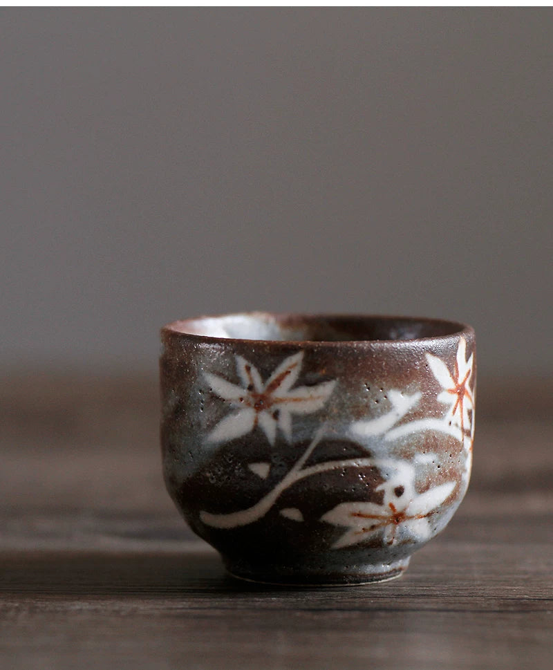 Dark brown ceramic tea cup decorated with white floral or leaf patterns on a dark wooden surface.