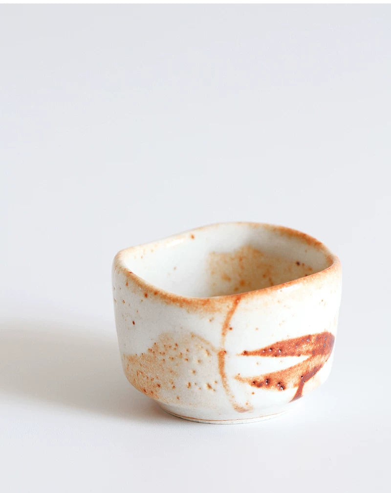 Single, low, rustic ceramic tea cup with white glaze and prominent orange-brown speckling and streaks.