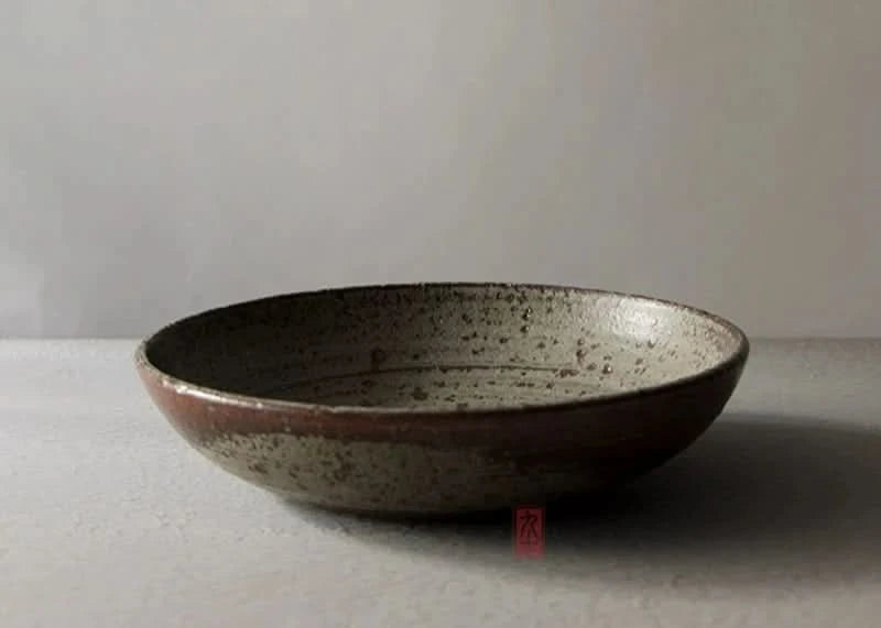 Handmade stoneware brown dinnerware bowl with speckled interior on a neutral surface.