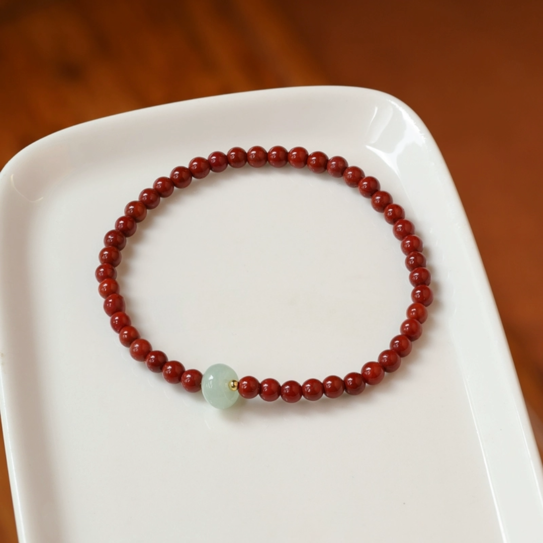 Jade Bracelet with Red Beads on white plate, featuring a central pale green jade bead and gold accent.