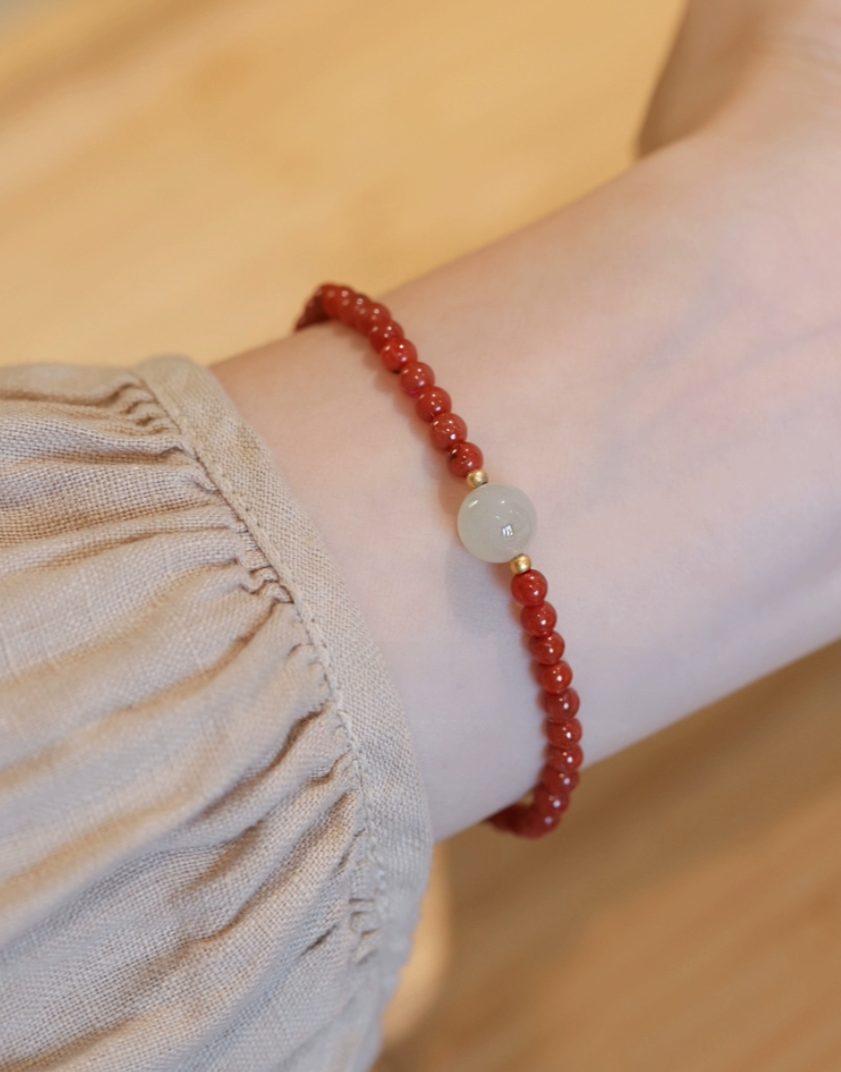 Jade bracelet with red beads and a single smooth jade stone on a wrist.